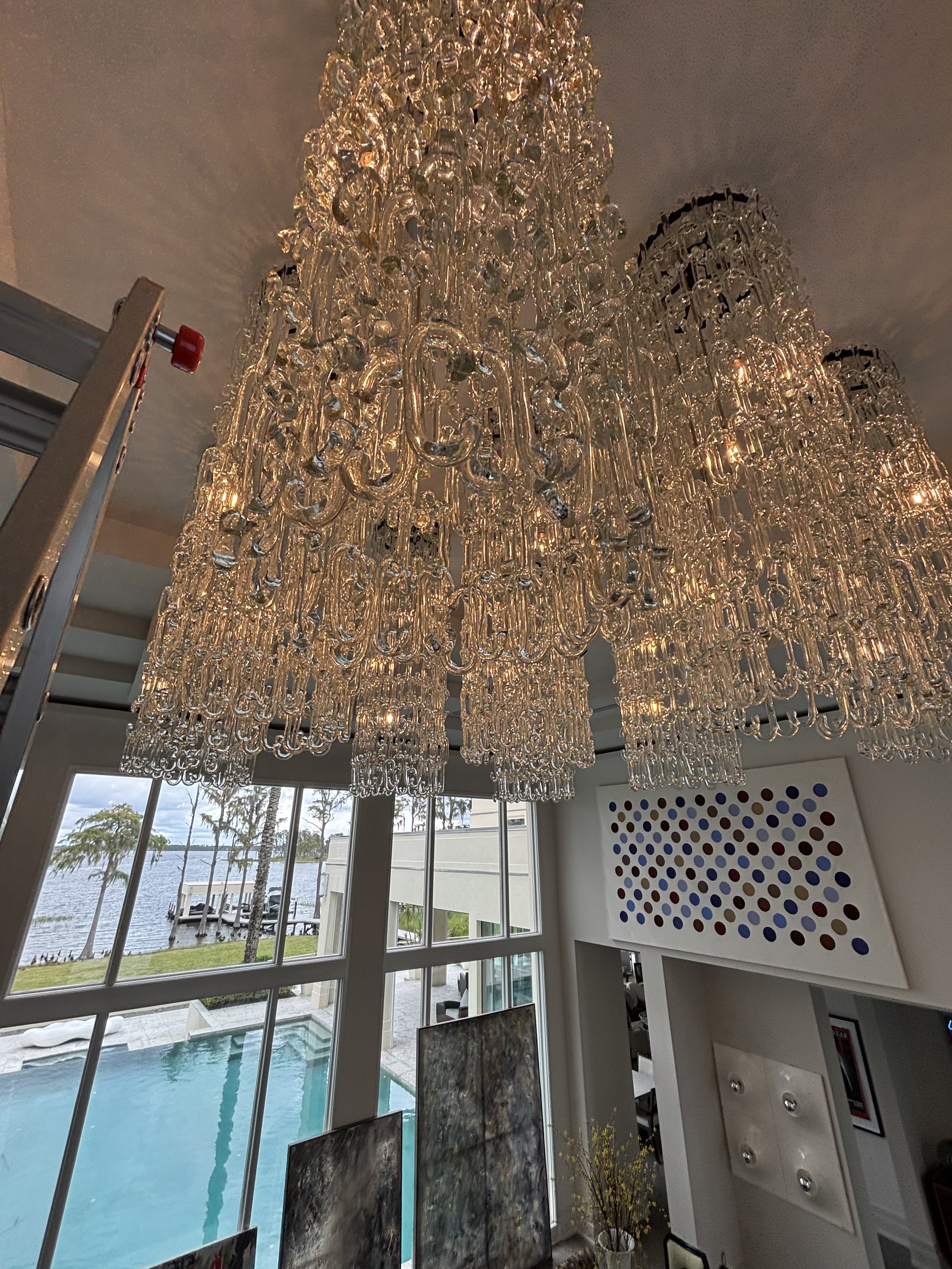 Handblown glass chain-link chandeliers lit up showing massive scale with ladder in upscale Orlando home