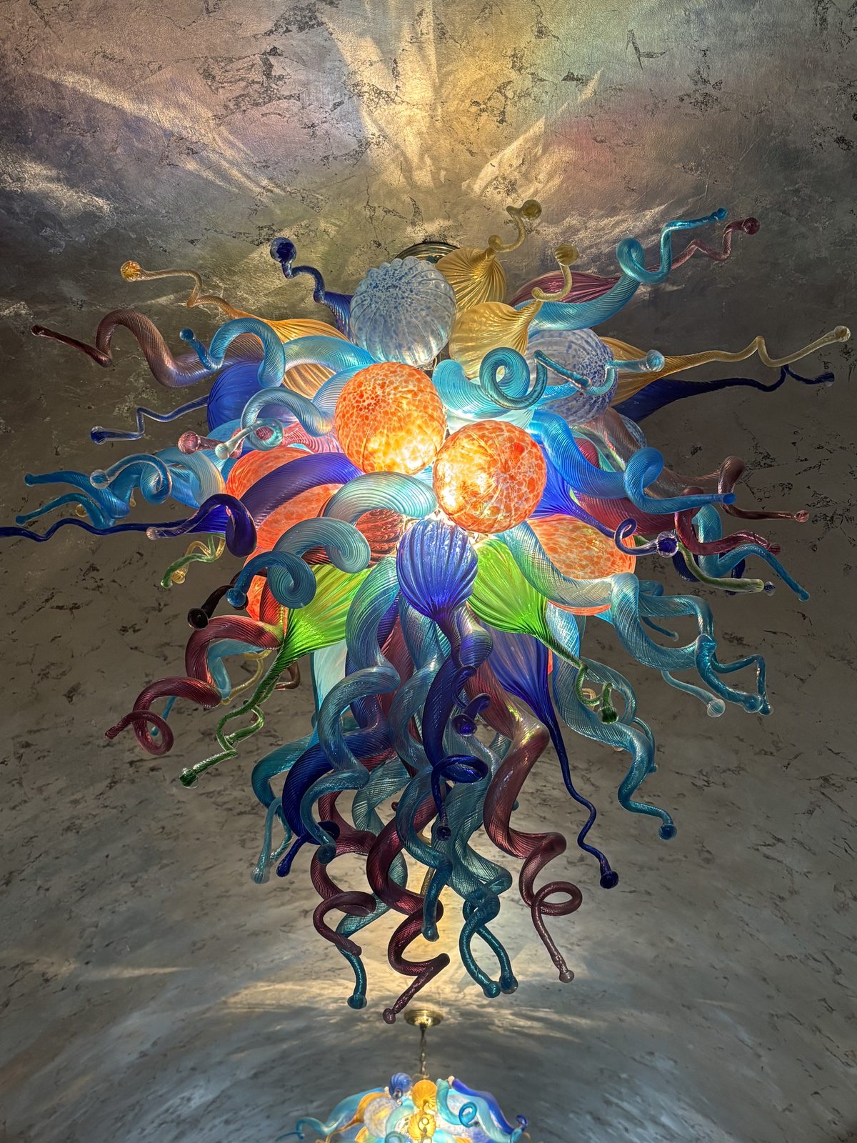 Chihuly handblown glass chandelier viewed from below — vibrant multicolor glass tendrils radiating outward