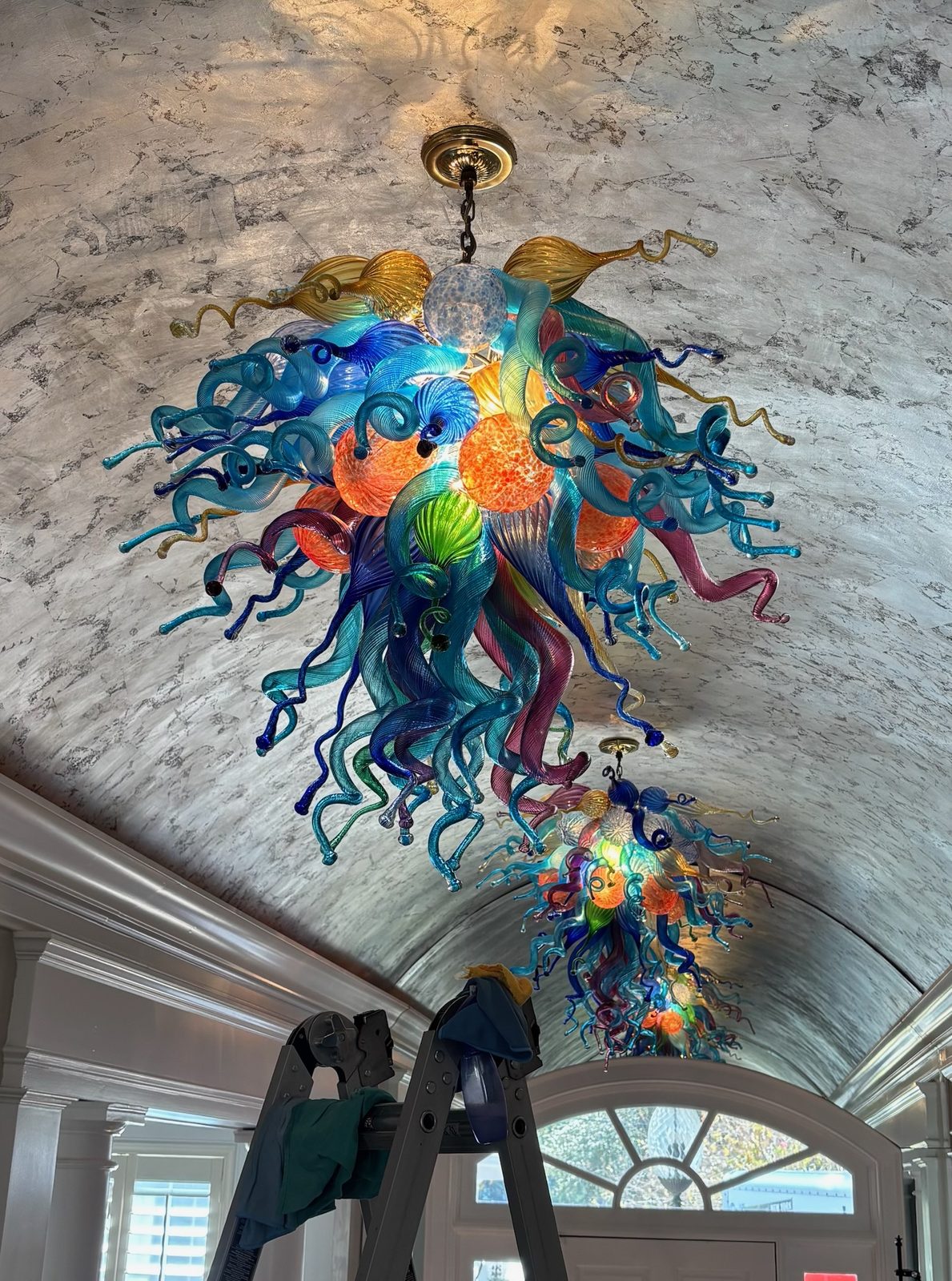Two Chihuly handblown glass chandeliers in a barrel-vaulted hallway with ladder between them