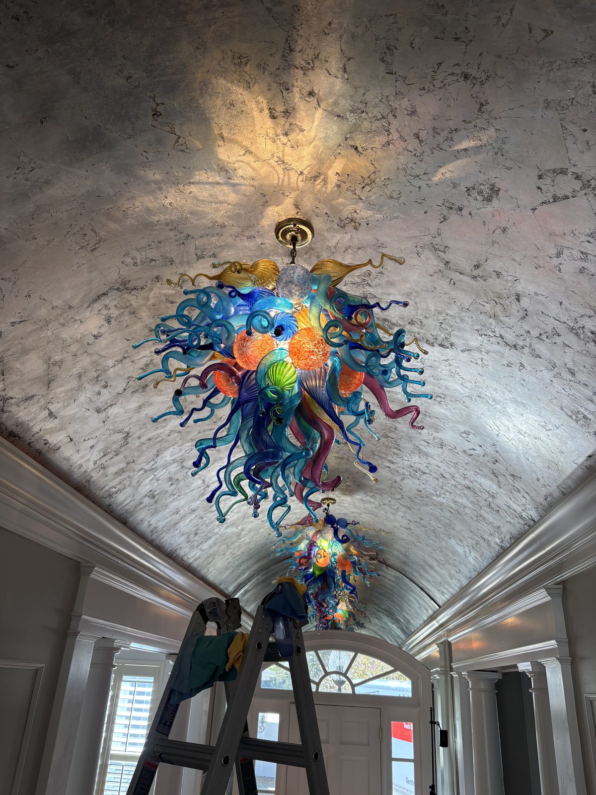 Chihuly glass chandelier with cleaning ladder positioned — showing scale and protruding glass elements